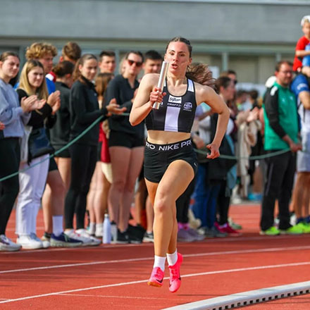 Jeune fille qui court sur une piste d'athlétisme avec un relais dans la main sur un sol rouge