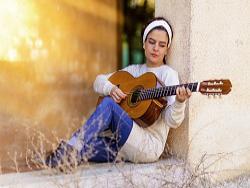 Une femme adossée à un rebord de fenêtre en train de jouer de la guitare