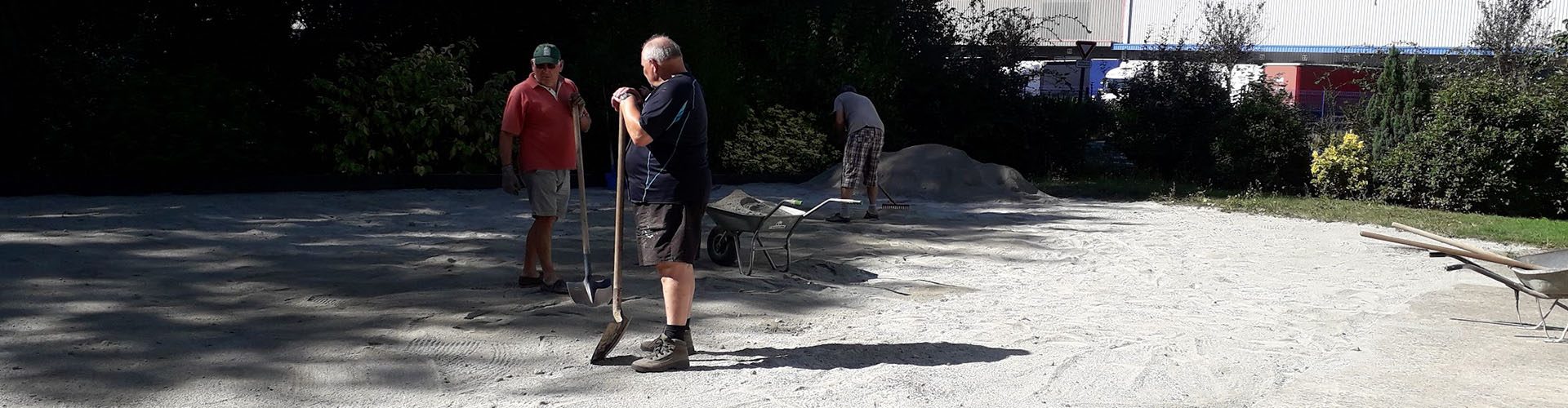 extérieur avec un ciel bleu, des arbres et la construction d'un terrain de pétanque à l'aide d'outil manuel